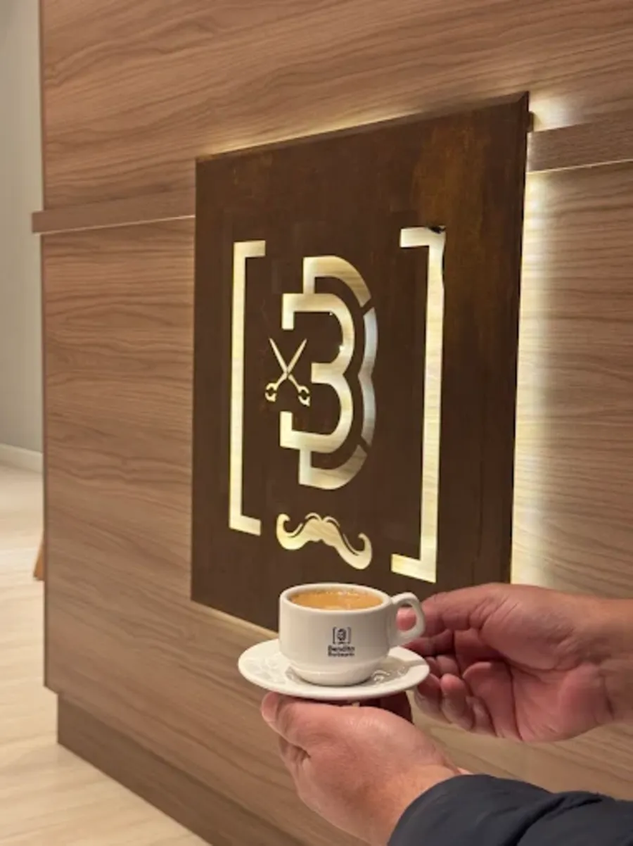 Xícara de café Bendita servida diante da logo dourada em madeira